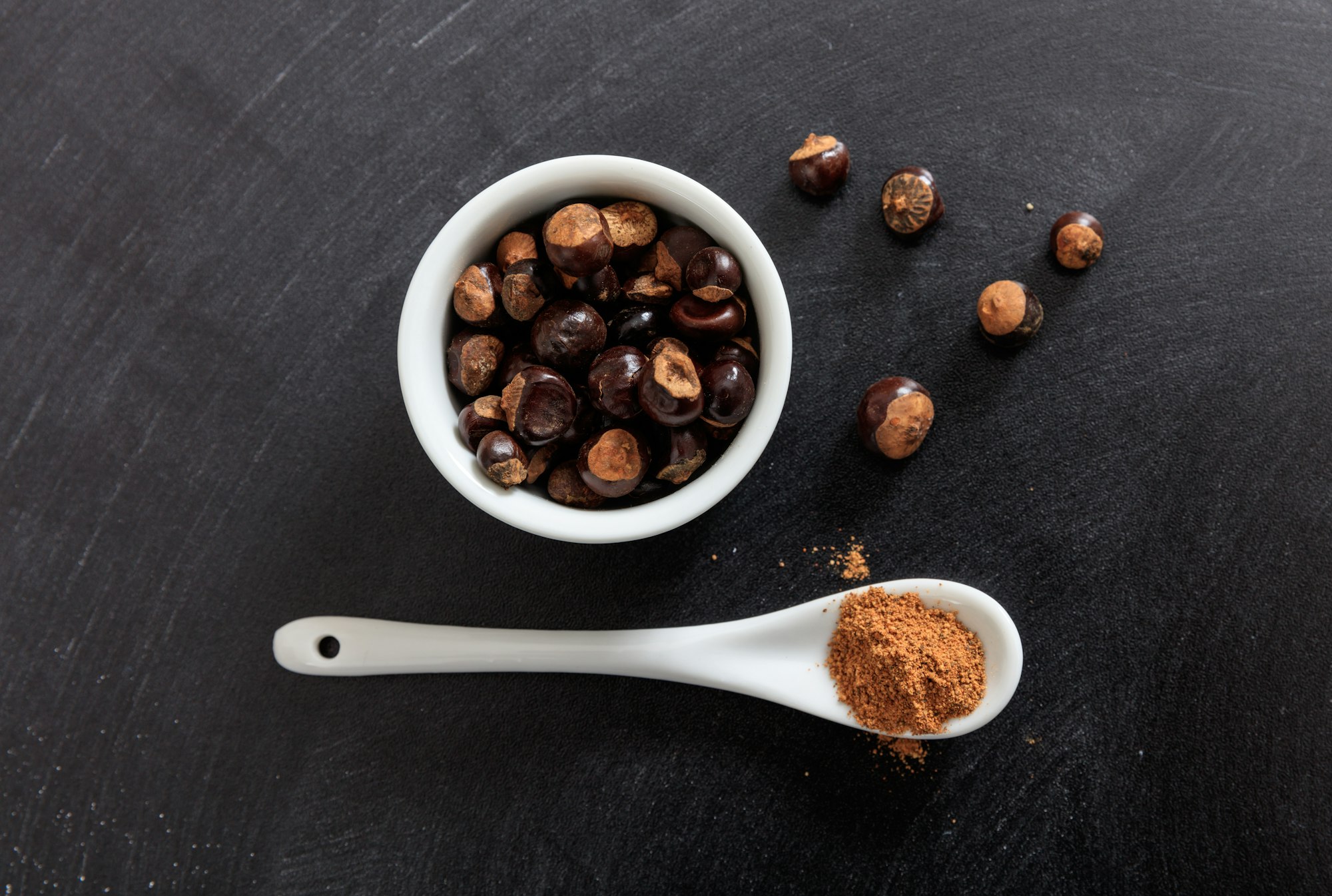 Guarana seeds and powder in porcelain bowl and spoon